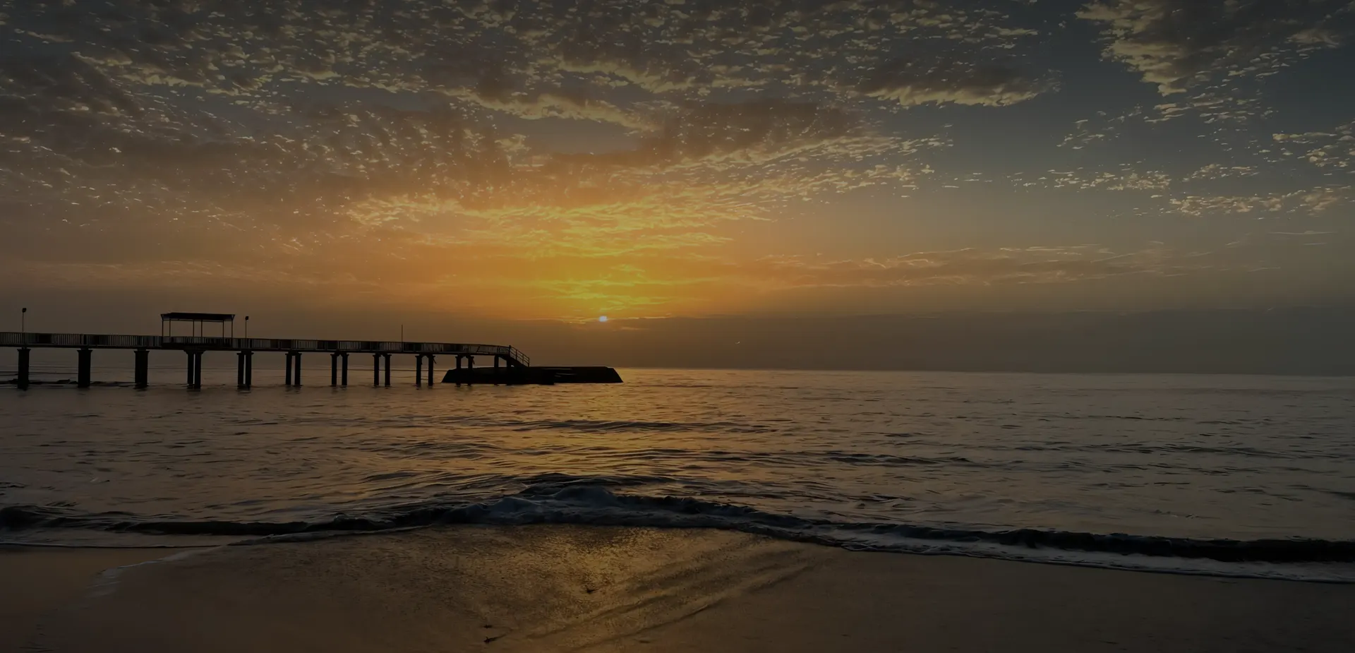 Sunrise over an empty pier — calm water, vast sky
